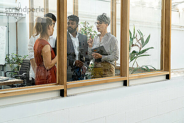 Geschäftsleute und Geschäftsfrauen diskutieren  während sie hinter dem Fenster stehen