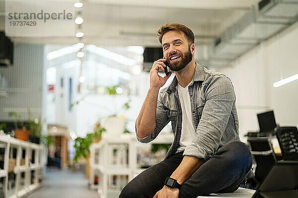 Männlicher Unternehmer telefoniert  während er am Tisch sitzt