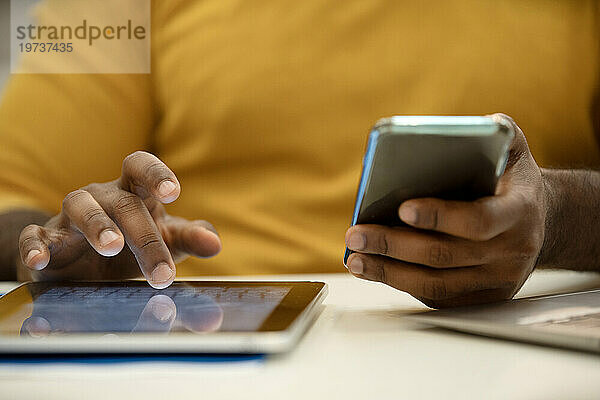 Nahaufnahme einer afroamerikanischen Männerhand  die ein digitales Tablet benutzt und ein Smartphone in der Hand hält