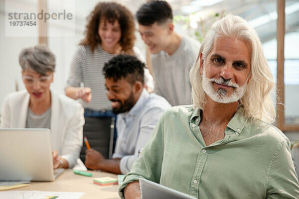 Industriedesigner blickt während eines Meetings in die Kamera  während er ein digitales Tablet in der Hand hält