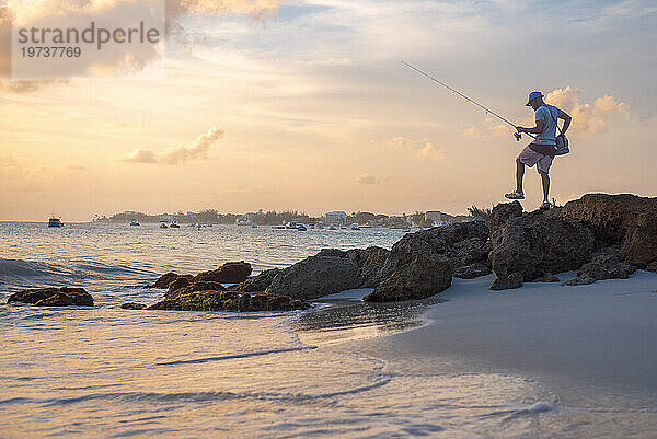 Ein lokaler Fischer bei Sonnenuntergang mit ruhigem Wasser und orangefarbenem Himmel an der Südküste von Barbados  Westindien  Karibik  Mittelamerika