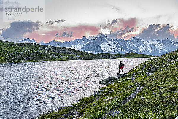 Wanderer steht am Ufer des Fenetre-Sees und bewundert den Sonnenuntergang über dem Massiv des Mont Blanc  Ferret-Tal  Kanton Wallis  Col du Grand-Saint-Bernard (St. Bernard-Pass)  Schweiz  Europa