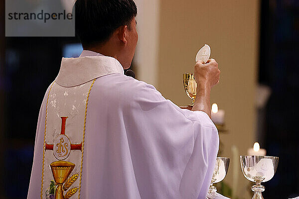 Back view of Priest with chasuble at Eucharist celebration  Sunday Mass  Elevation of the Host  St. Nicholas Cathedral  Dalat  Vietnam  Indochina  Southeast Asia  Asia