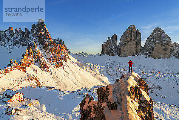 Rückansicht eines Wanderers  der die Drei Zinnen von der Spitze eines riesigen Felsens aus bewundert  Winteransicht  Sexten  Dolomiten  Südtirol  Italien  Europa