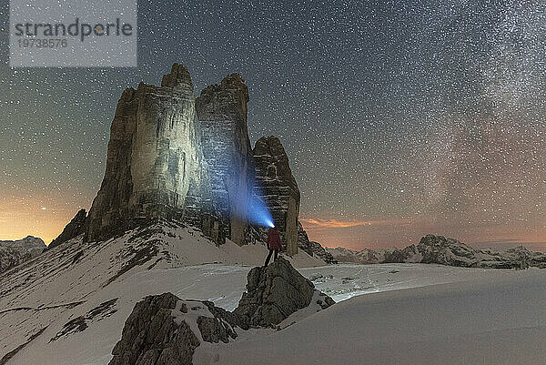 Wanderer mit Stirnlampe blickt in einer sternenklaren Nacht mit der Milchstraße auf die Drei Zinnen  Winteransicht  Drei Zinnen (Lavaredo-Gipfel)  Sexten  Dolomiten  Südtirol  Italien  Europa