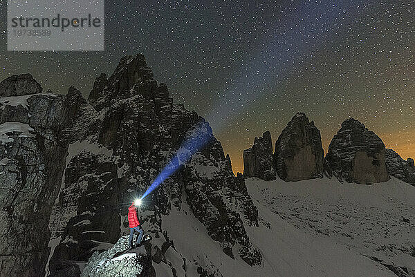 Mann mit Stirnlampe beleuchtet den Sternenhimmel über dem verschneiten Paterns und den Drei Zinnen  Sexten  Dolomiten  Südtirol  Italien  Europa