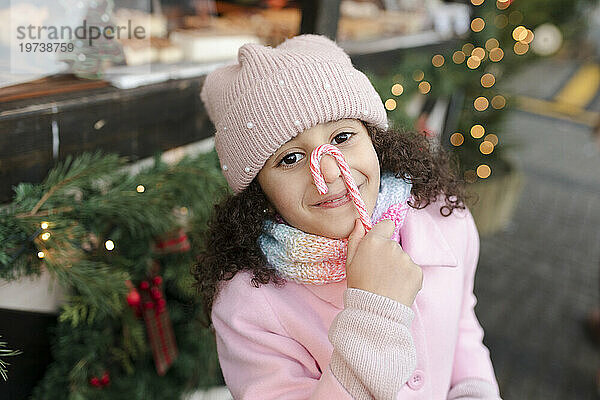Smiling girl holding candy cane over face at Christmas market