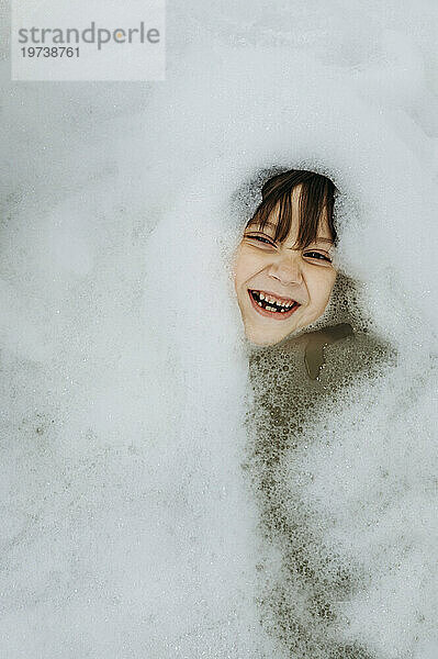 Cheerful boy amidst soap sud in bathtub