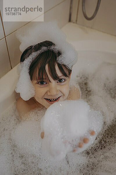 Junge spielt zu Hause mit Seifenlauge in der Badewanne