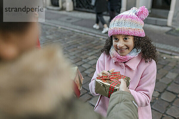Brother giving gift box to smiling sister at street