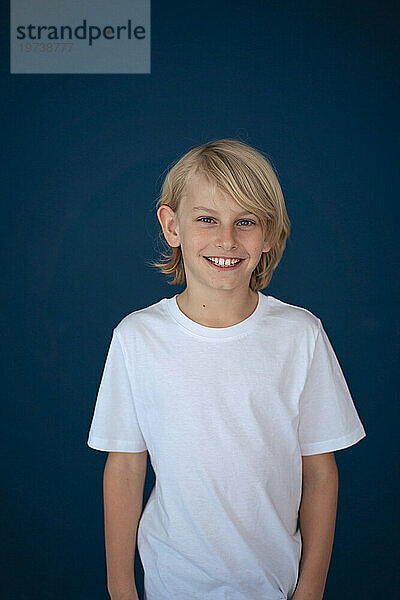 Smiling blond boy standing against blue background