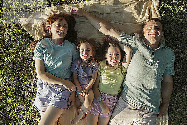 Lächelnde Eltern mit Töchtern  die auf einer Decke im Park liegen