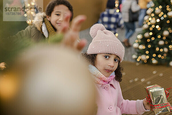 Girl holding gift box with brother enjoying at Christmas market