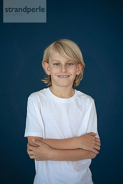 Happy boy standing with arms crossed against blue background