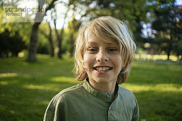 Smiling blond boy in front of trees at park