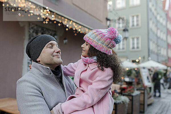 Lächelnder Vater trägt Tochter auf dem Weihnachtsmarkt