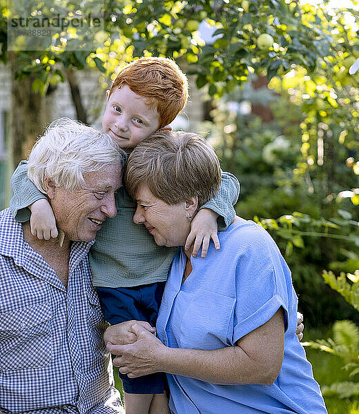 Junge umarmt Großeltern im Garten