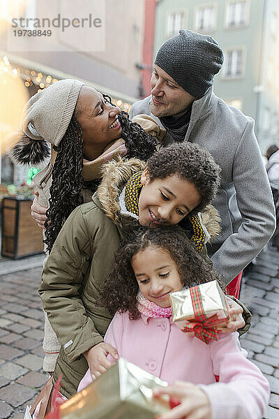 Glückliche Eltern mit Kindern  die Geschenkboxen auf dem Weihnachtsmarkt halten