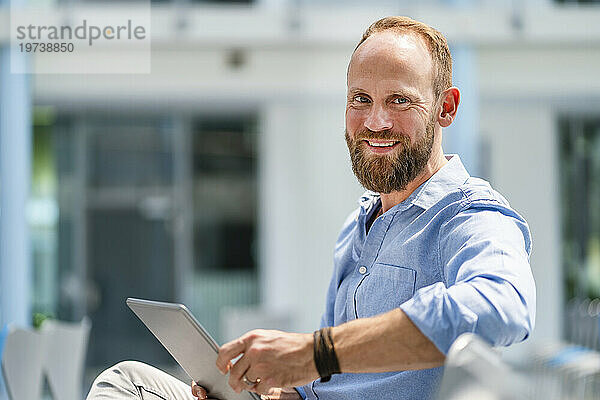 Geschäftsmann sitzt im Firmenauditorium und nutzt digitales Tablet