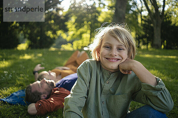 Lächelnder Junge mit Eltern im Hintergrund  der sich im Park entspannt