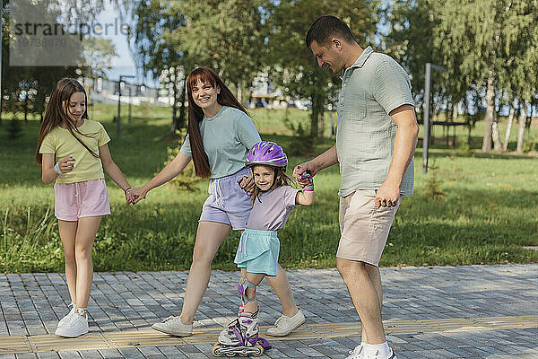 Lächelndes Mädchen beim Rollschuhlaufen mit Eltern und Schwester im Park