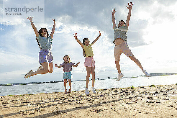 Fröhliche Eltern mit Töchtern  die am Strand springen
