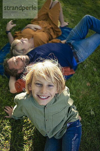 Lächelnder Junge mit Eltern  die sich im Gras entspannen