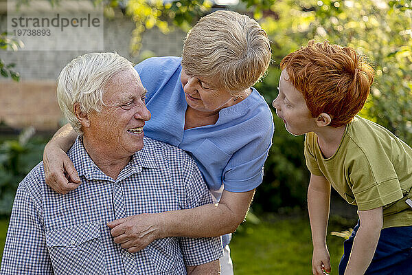 Enkel neben Großmutter mit Arm um älteren Mann im Garten