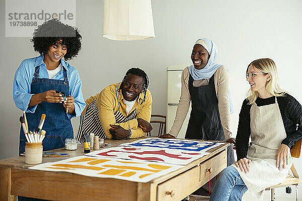 Künstler lachen mit Gemälden auf dem Schreibtisch im Studio