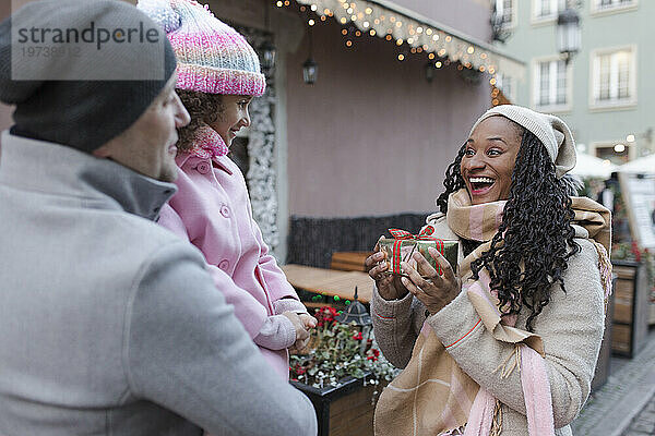 Glücklicher Vater und Tochter mit Mutter  die Geschenkbox auf dem Weihnachtsmarkt hält