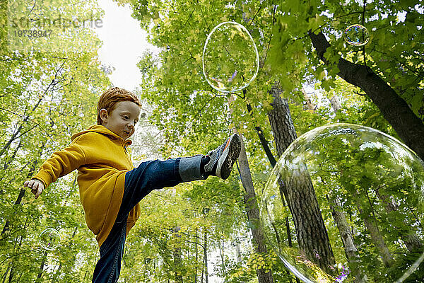 Verspielter Junge  der im Herbstwald Seifenblasen tritt