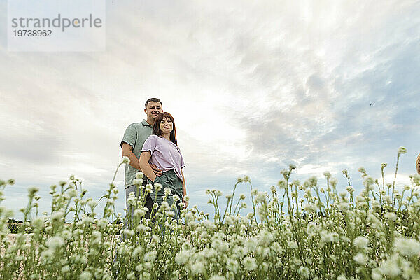 Glückliches Paar steht auf einem Blumenfeld unter dem Himmel
