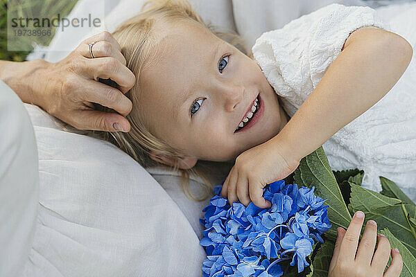 Glückliches Mädchen mit blauen Blumen  das auf dem Schoß der Mutter liegt