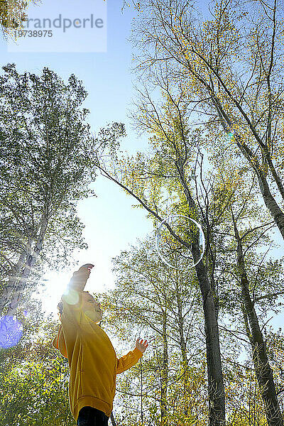 Fröhlicher Junge  der an einem sonnigen Tag Seifenblasen im Herbstwald jagt