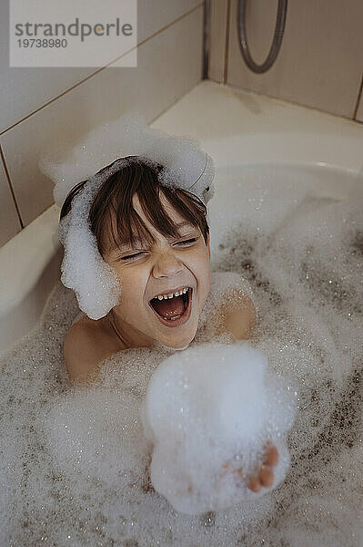 Fröhlicher Junge mit Seifenlauge in der Badewanne zu Hause