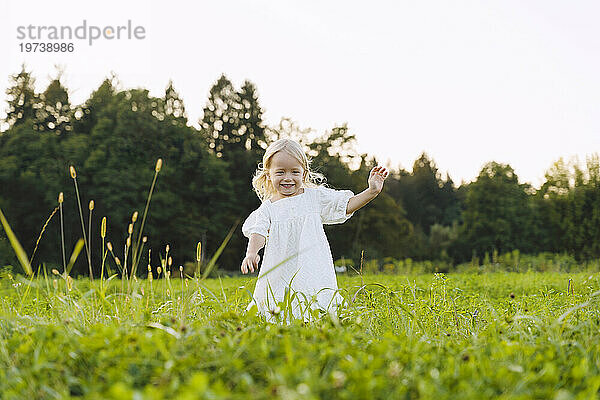 Smiling blond girl running in front of trees