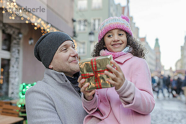 Lächelnder Vater mit Tochter hält Geschenk auf dem Weihnachtsmarkt