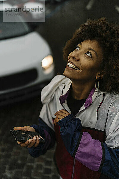 Glückliche junge Frau mit Smartphone im Regen