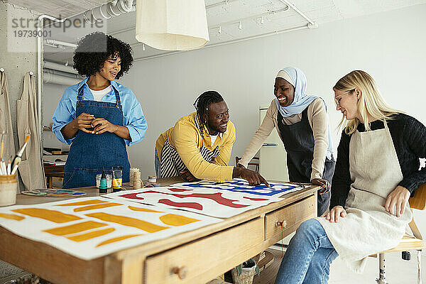 Lächelnde Künstler diskutieren über Gemälde auf dem Schreibtisch im Atelier