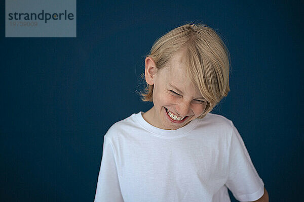 Cheerful boy laughing against blue background