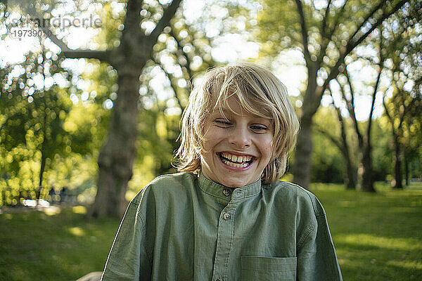 Happy blond boy in front of trees at park
