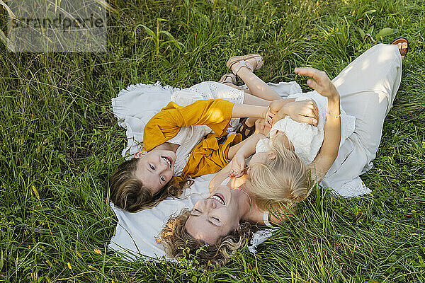 Fröhliche Mutter hat Spaß mit Töchtern  die im Gras liegen