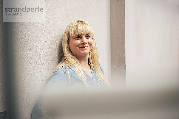 Smiling blond woman leaning on wall