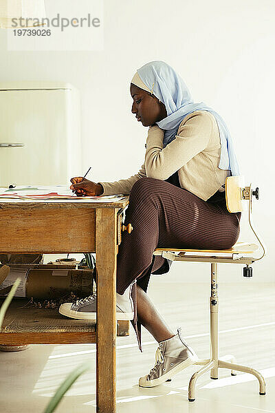 Artist wearing headscarf painting with brush at desk in studio