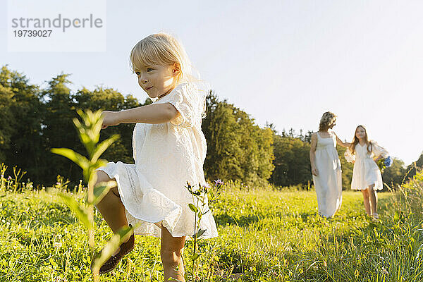 Mädchen geht mit Mutter und Schwester im Hintergrund auf dem Feld spazieren
