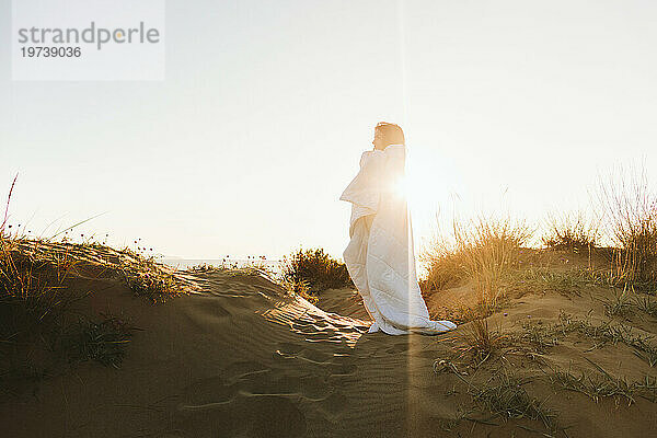 Frau  in eine Decke gehüllt  steht an einem sonnigen Tag am Strand