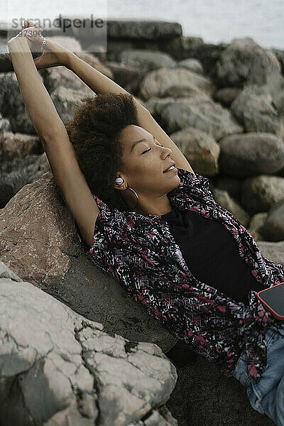 Junge Frau mit geschlossenen Augen und erhobenen Armen entspannt sich auf Felsen