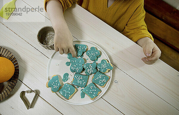 Junge dekoriert Kekse auf Teller am Esstisch