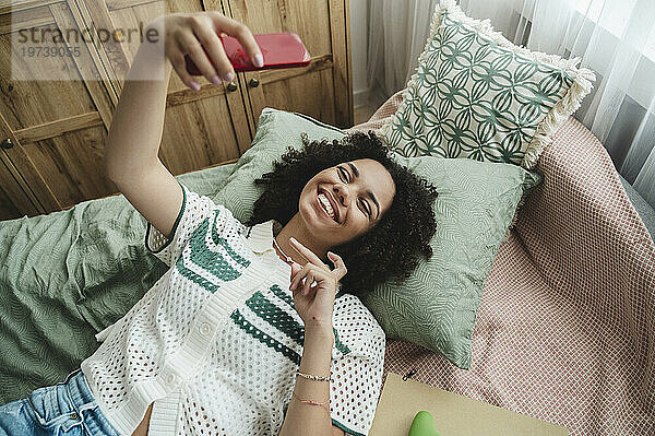 Fröhliches Teenager-Mädchen  das zu Hause im Bett ein Selfie mit dem Smartphone macht