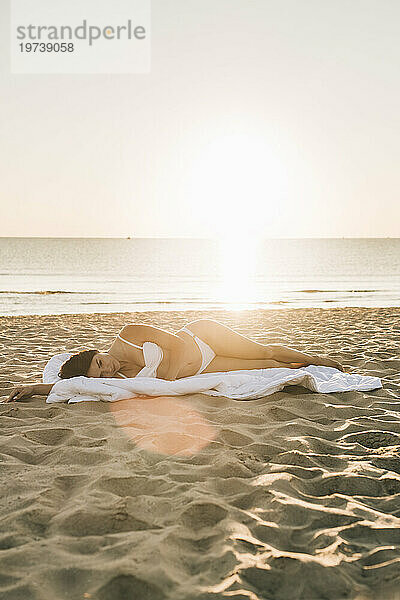 Frau liegt auf einer Decke am Strand unter freiem Himmel